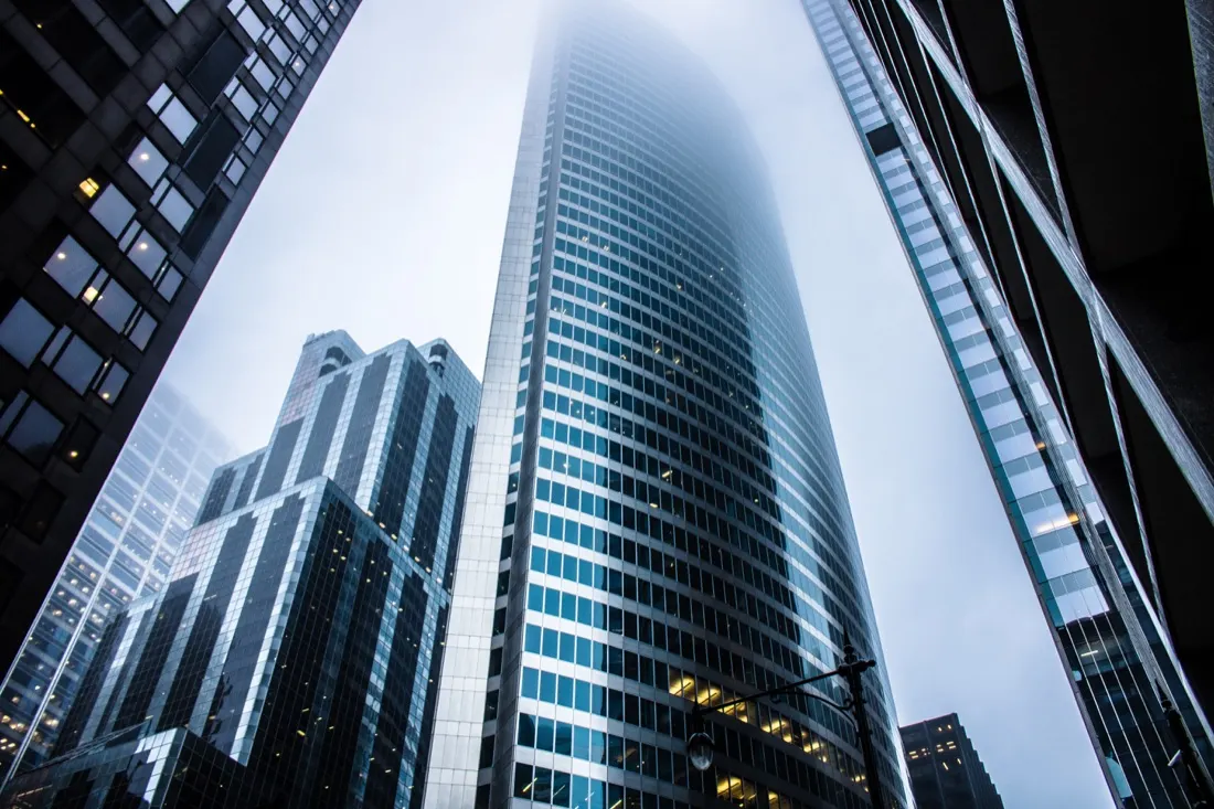 Low-angle view of an office skyscraper disappearing into fog, illustrating reluctance to return to the office post-covid