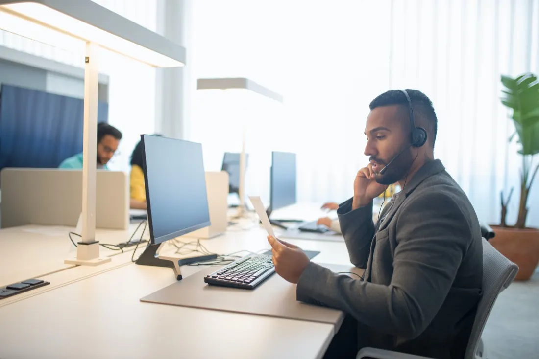 A contact centre agent wearing a headset while reviewing a note at his desk, illustrating winning over contact centre sceptics