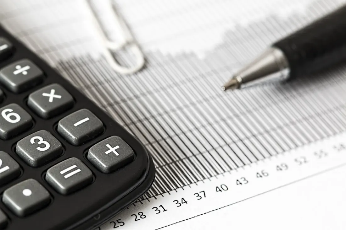 A calculator, paperclip and pen resting on a printed financial ledger, illustrating how tax systems affect multinational companies