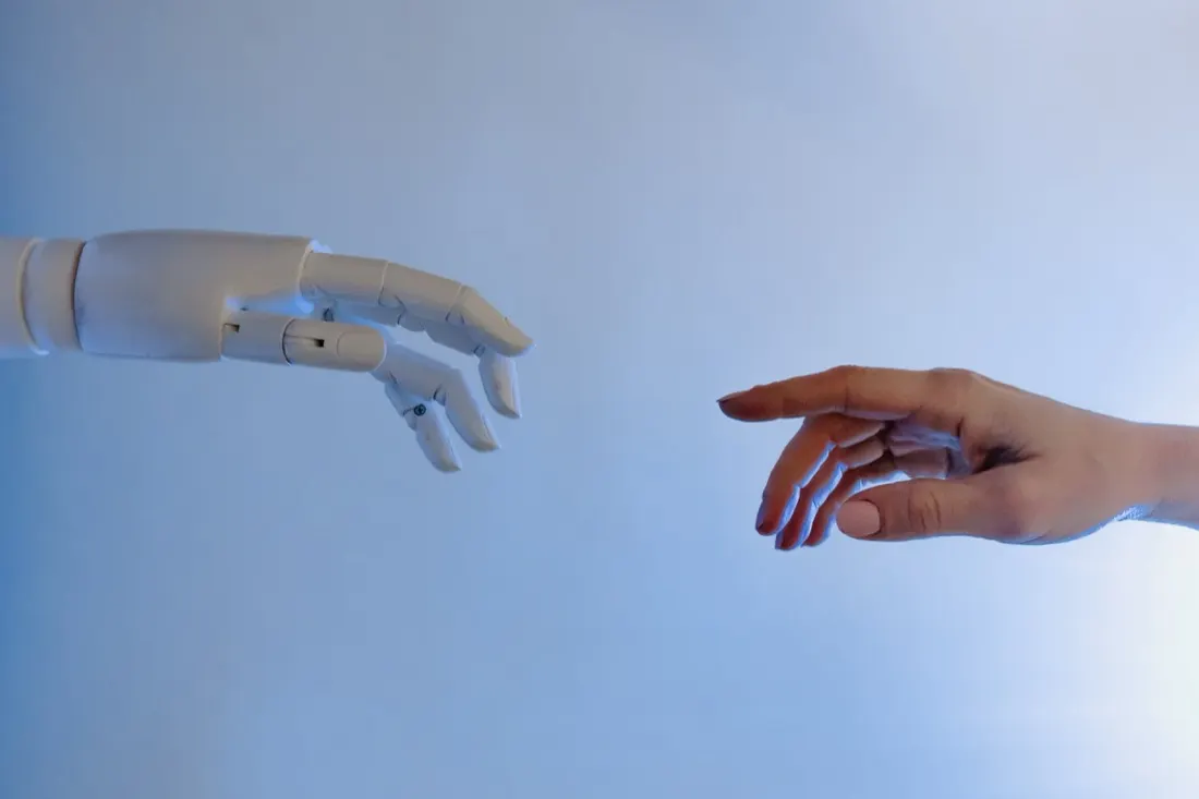 A robotic hand reaching towards a human hand, symbolising AI in the workplace