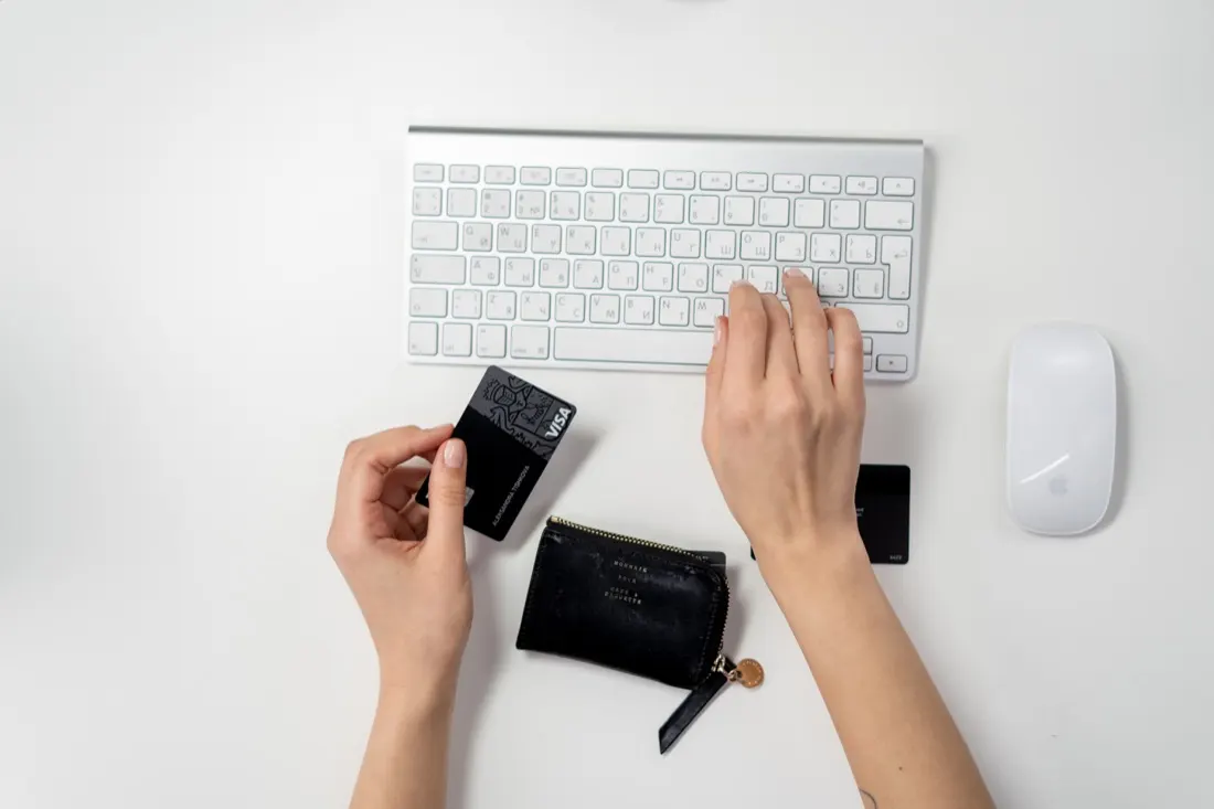 Hands holding a bank card and wallet beside a keyboard, illustrating payment fraud liability in contact centres