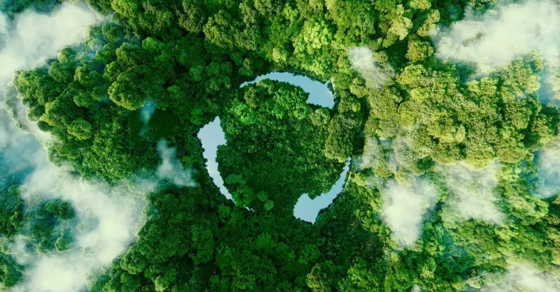 Aerial view of a lush forest with a lake shaped like a recycling symbol, representing green initiatives
