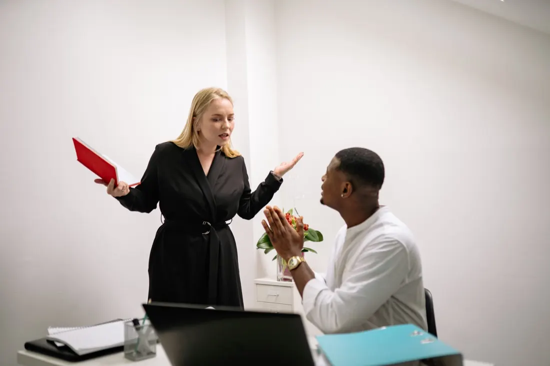 Woman gesturing while speaking to a seated man holding a folder in an office, illustrating manager pay disputes