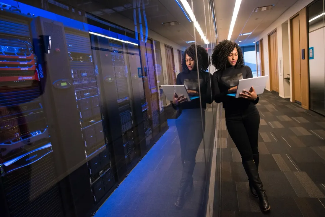 A woman reviewing a tablet beside a mirrored wall of server racks in a data centre corridor, illustrating the choice between SOC and SIEM