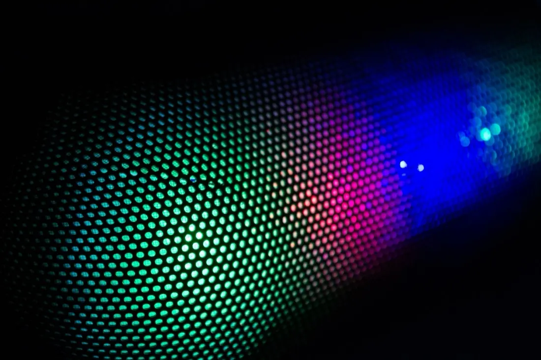 An abstract close-up of a curved grid of glowing green, pink and blue lights, illustrating the pace of digital disruption