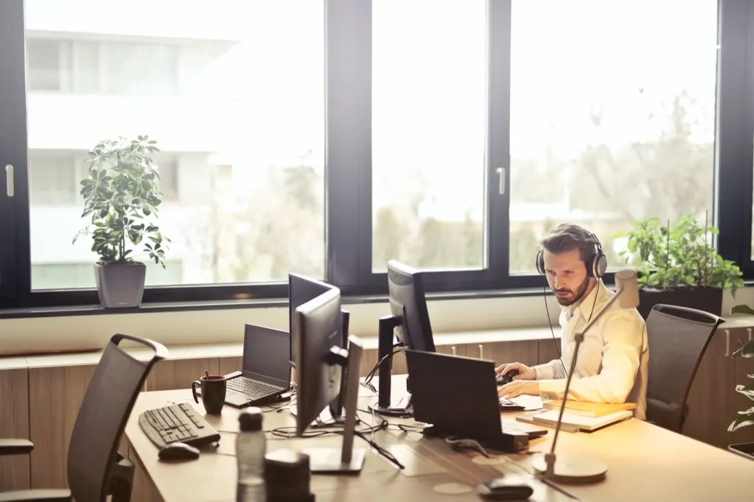 Man wearing a headset working across multiple monitors in a bright office, illustrating the future of customer service