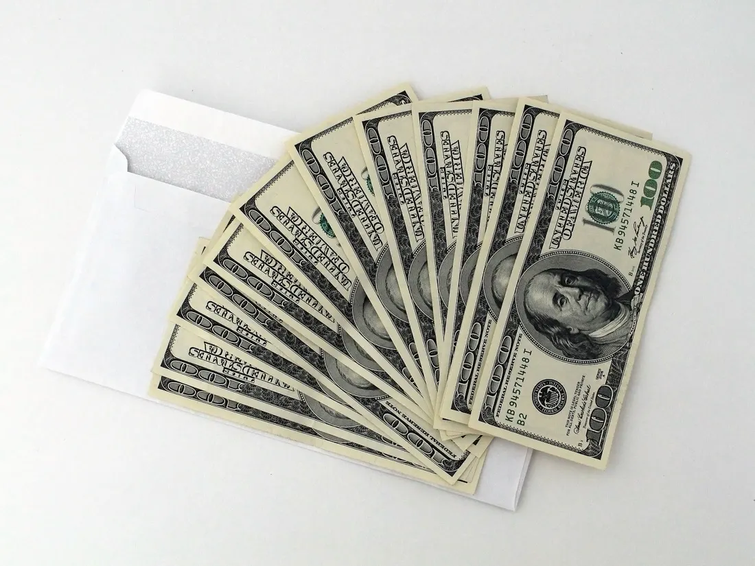 Fanned stack of hundred-dollar notes emerging from a white envelope, referencing donations to anti-climate politicians