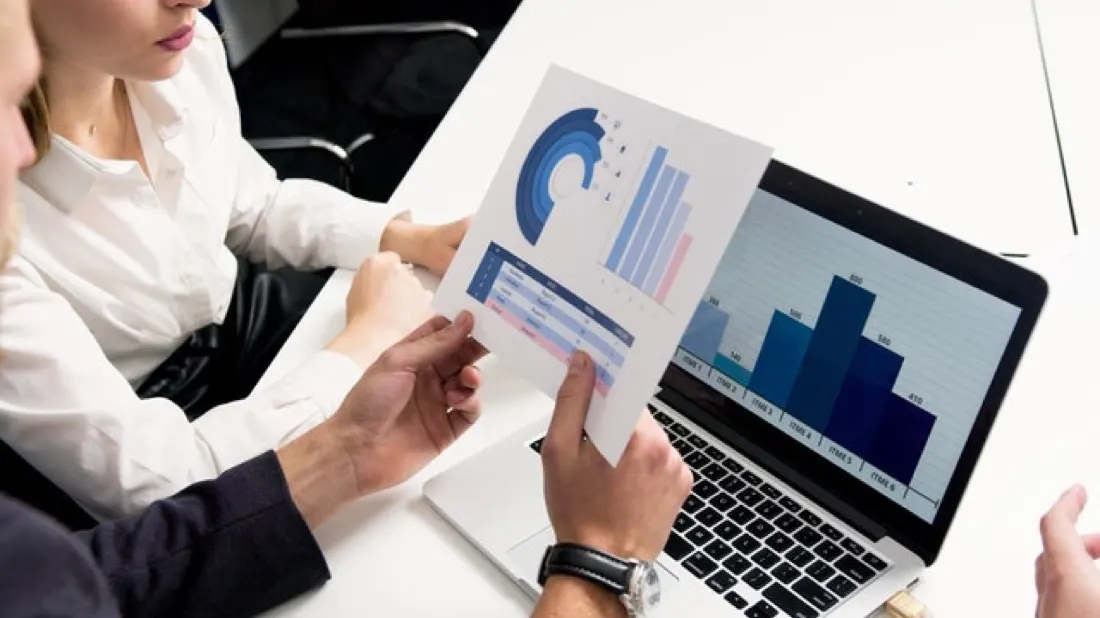 Two colleagues reviewing a printed bar chart beside a laptop showing similar data, illustrating investor confidence