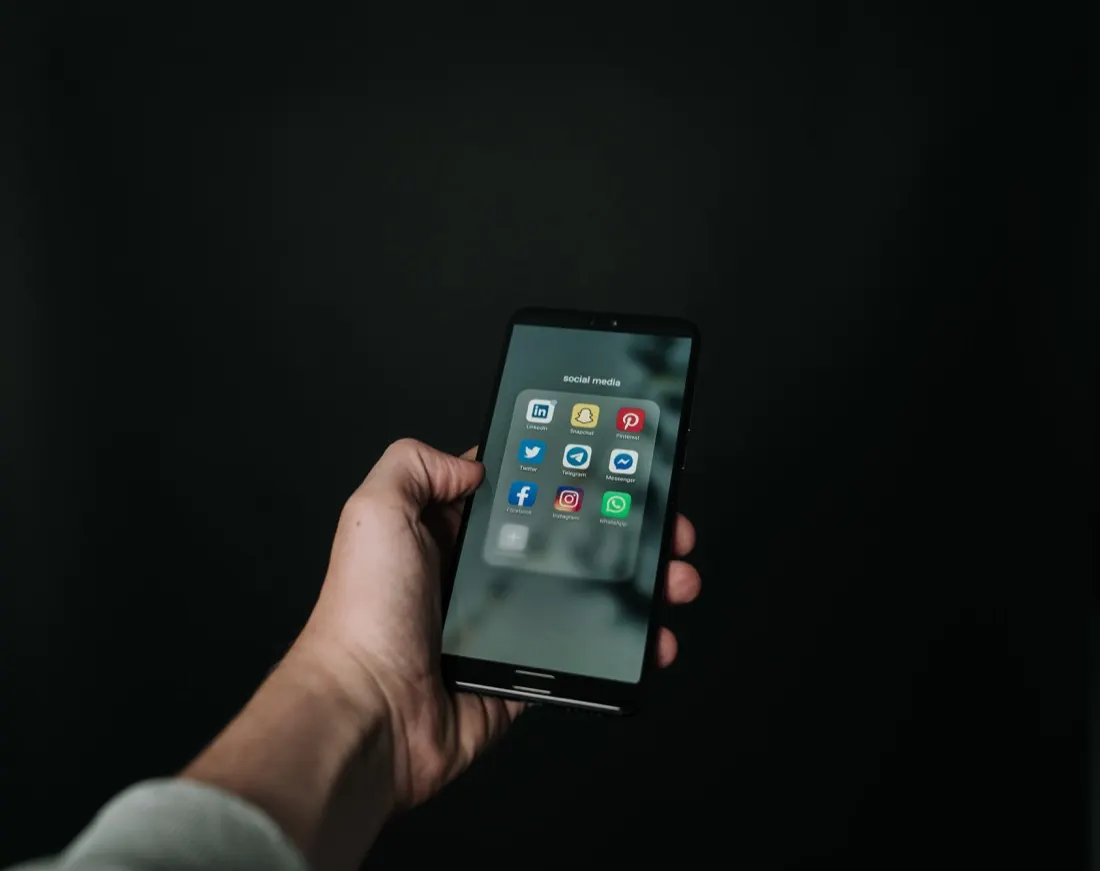 A hand holding a smartphone showing social media app icons against a dark background, illustrating social media candidate screening