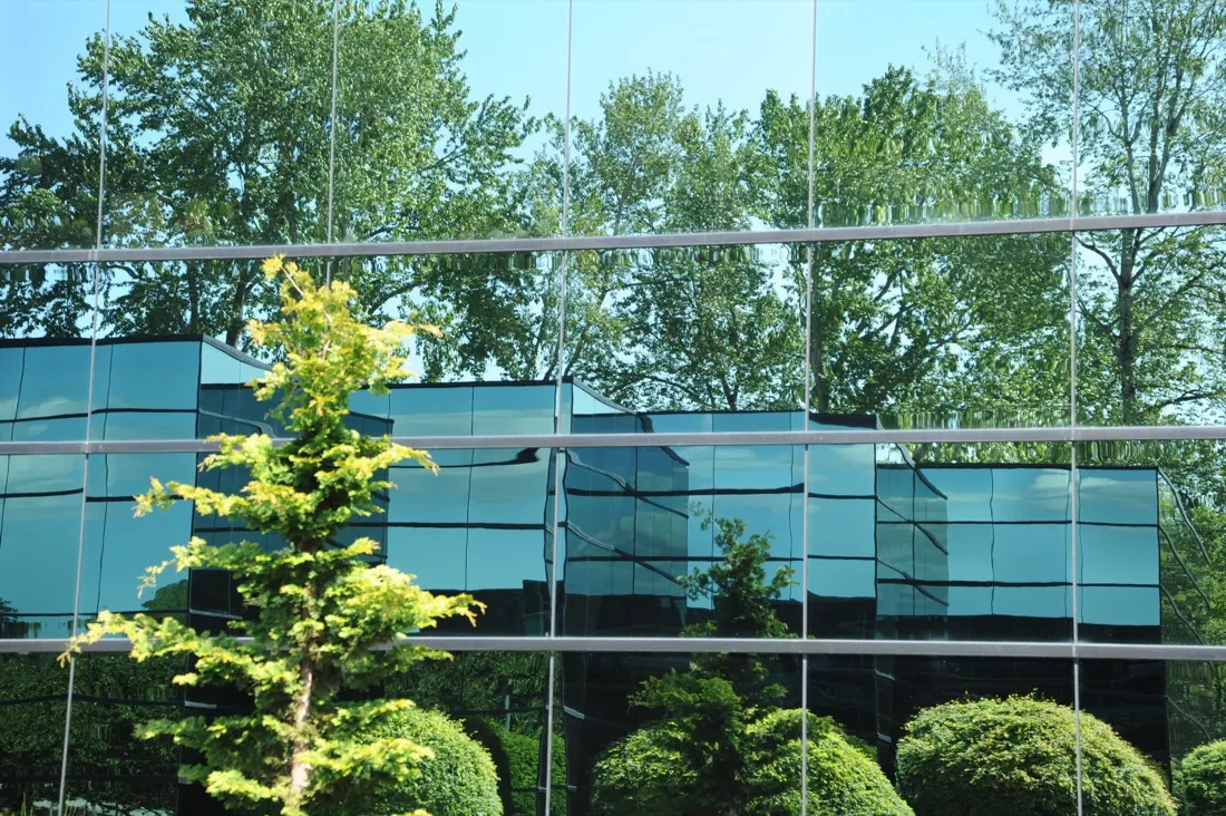 Glass office building reflecting surrounding trees and greenery, illustrating green spaces in the workplace