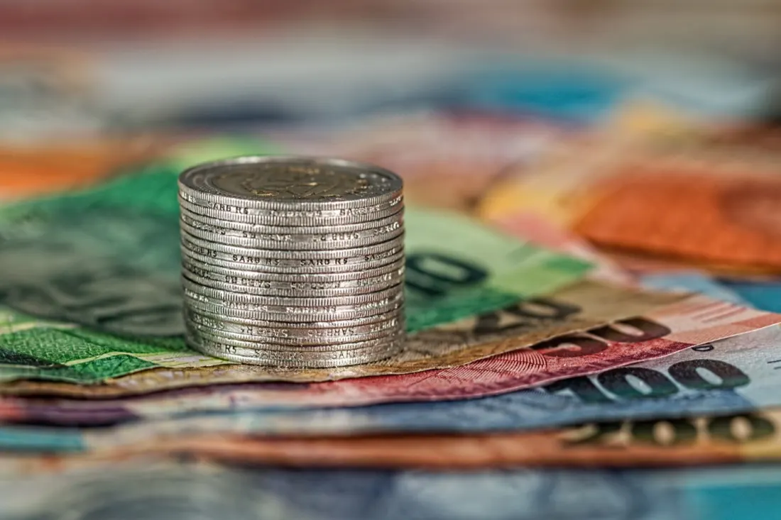 Stack of coins resting on colourful foreign banknotes, illustrating economic diplomacy amid global tensions