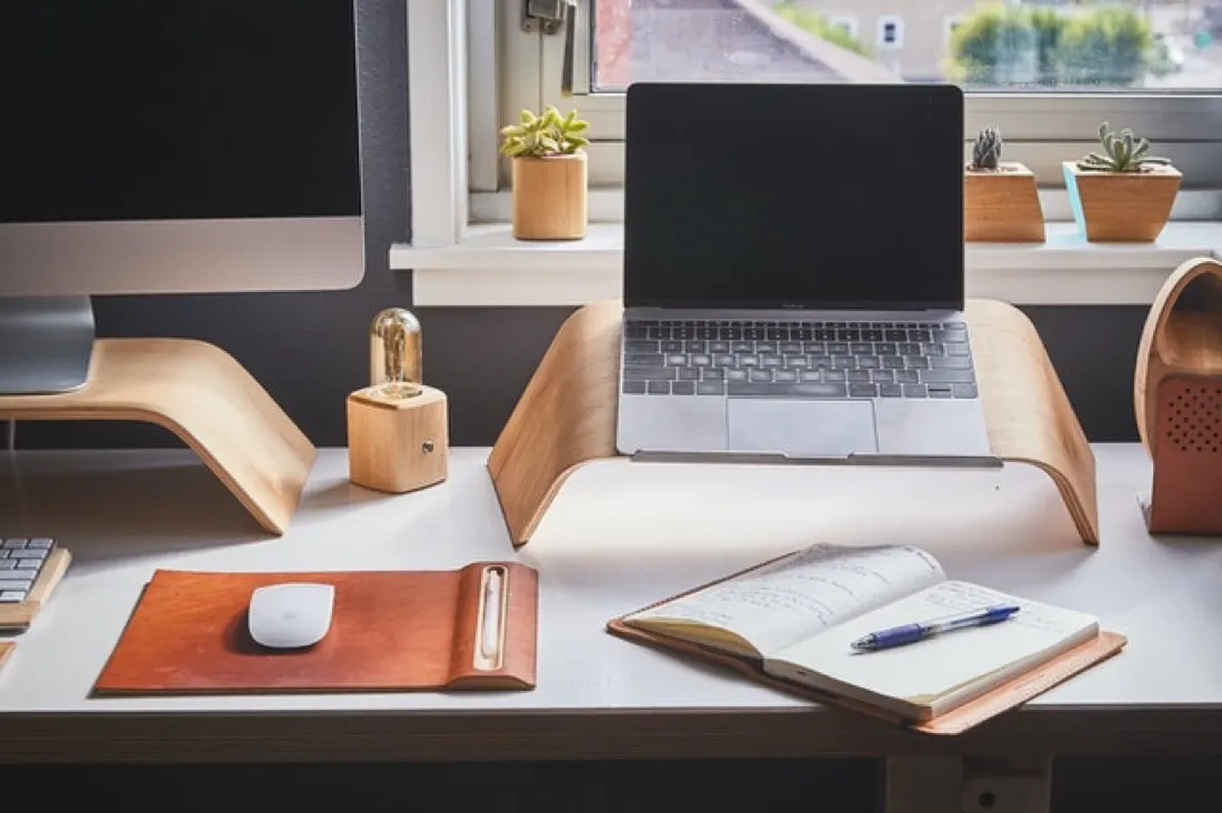 A home desk setup with a laptop, monitor stand, notebook and succulents, illustrating remote working needs
