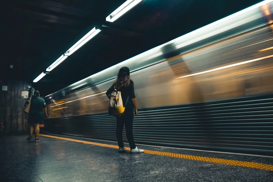 A commuter waiting on a platform as a train speeds past in a blur, illustrating the return of the morning commute