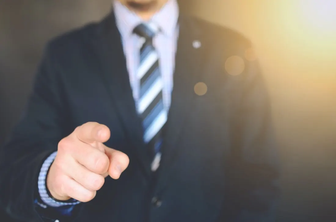 Businessman in a suit pointing directly at the camera, illustrating the drive behind global talent acquisition