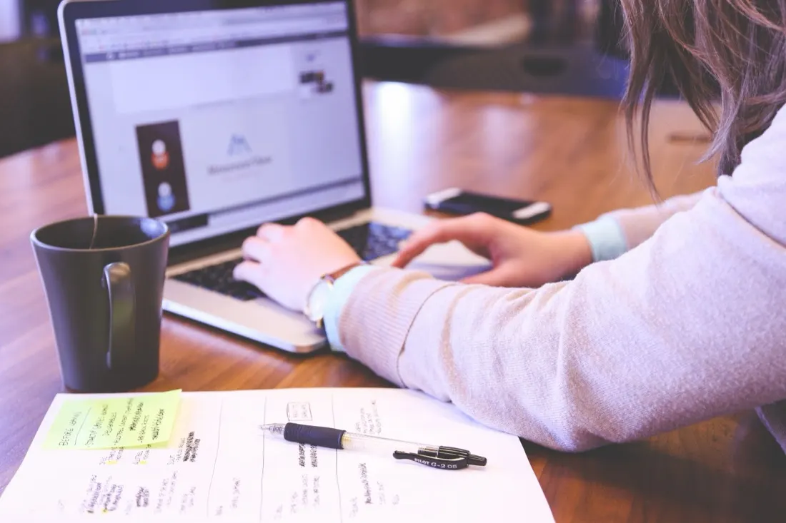 A woman working on a laptop at a wooden table with coffee and handwritten notes nearby, illustrating the top talent trends