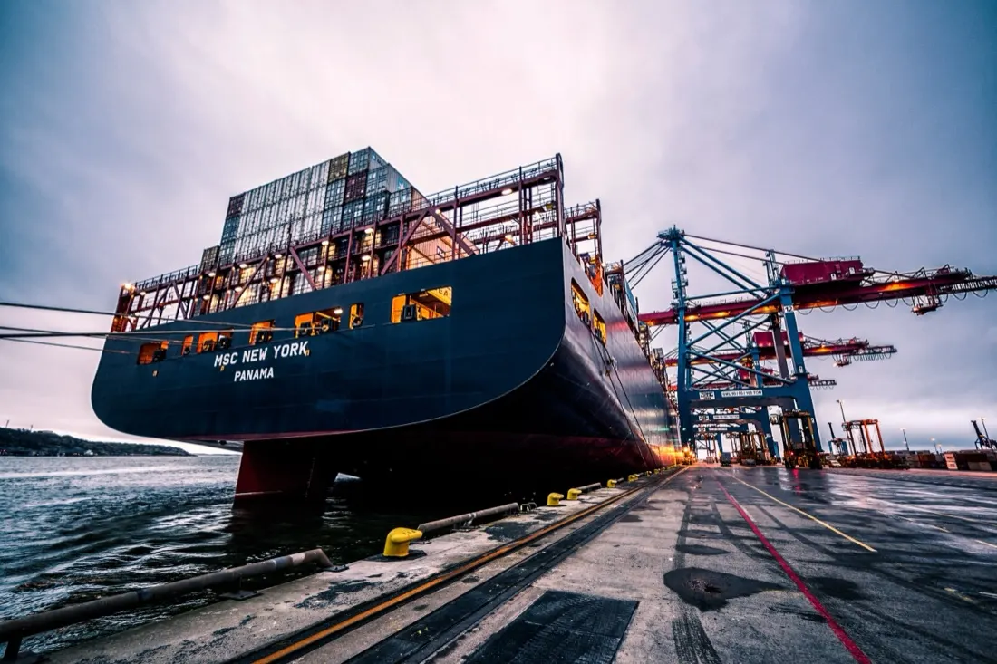 A container ship docked at a busy port terminal, illustrating the transformation of port logistics
