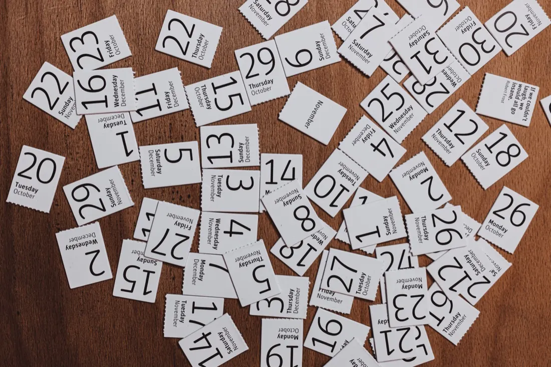 Scattered daily calendar date cards spread across a wooden table, illustrating attendance bonuses