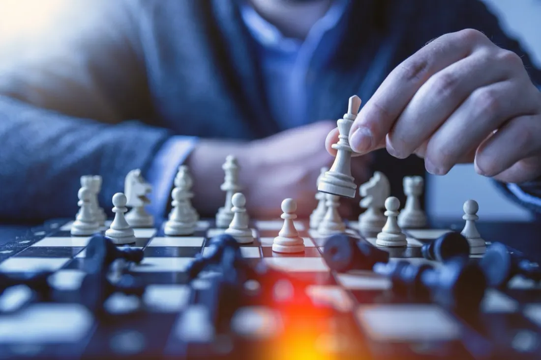 Hand moving a white king chess piece across the board, symbolising a winning business strategy