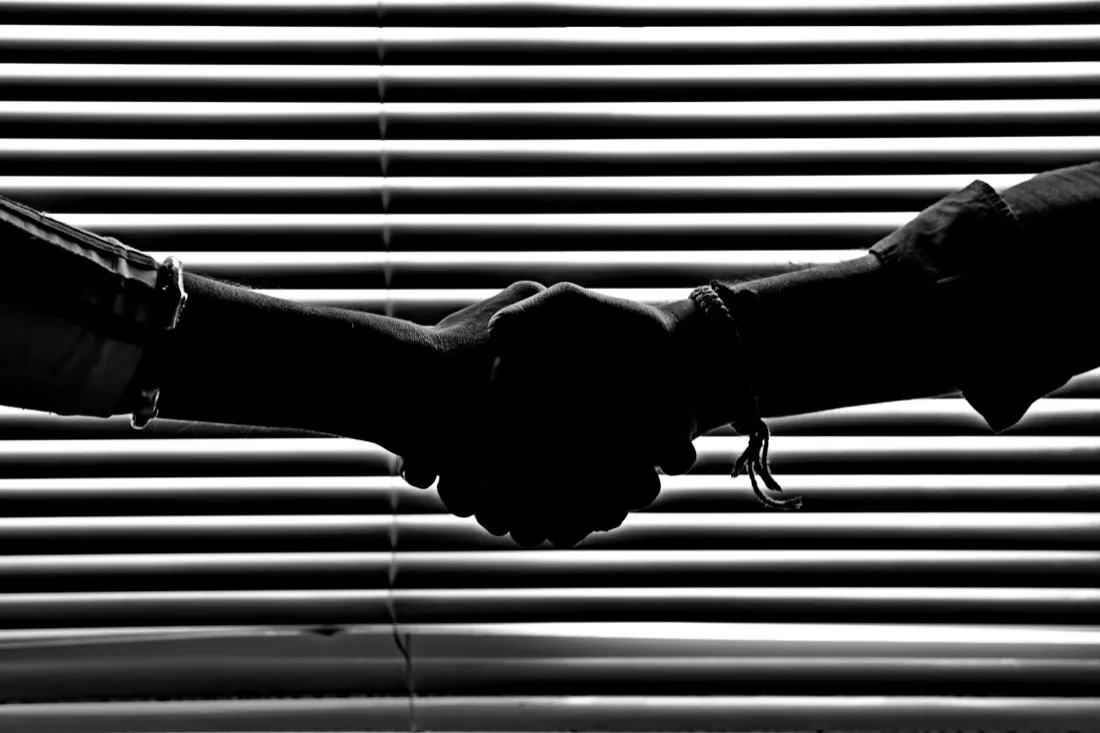 Silhouetted handshake in front of venetian blinds, symbolising a deal requiring strong internal controls