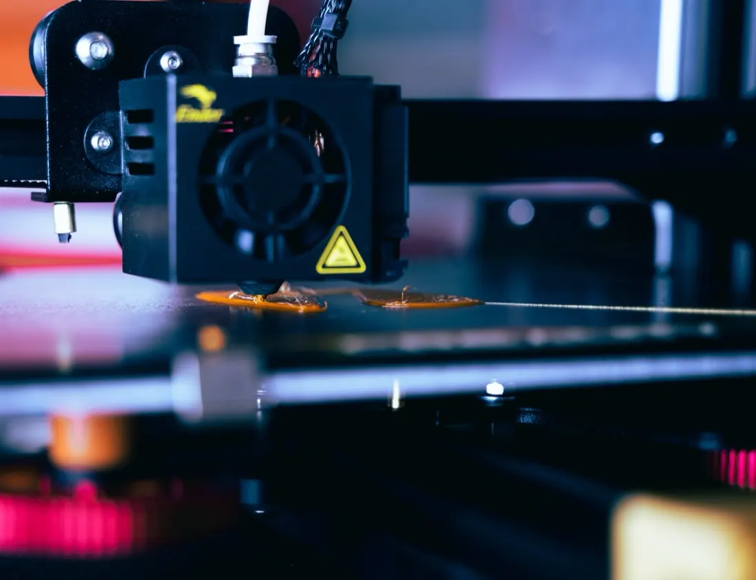 Close-up of a 3D printer nozzle extruding orange plastic parts, illustrating 3D printing for spare parts supply chains