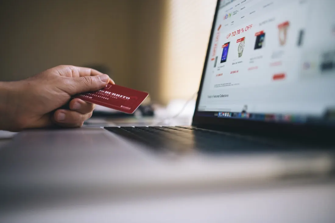 Hand holding a credit card beside a laptop showing an online sale, illustrating the steady pulse of consumer sentiment